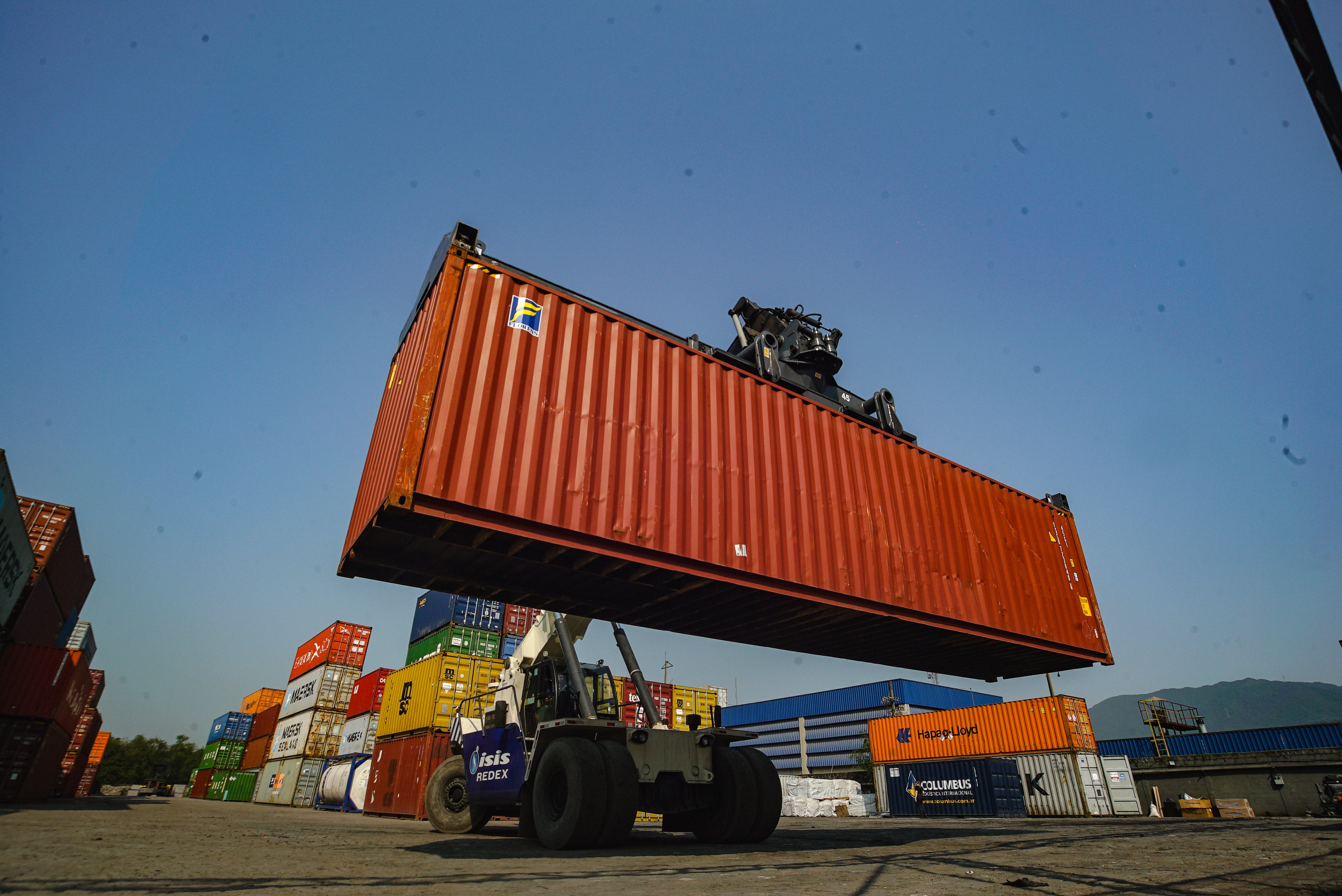 Contêiner de carga sendo movimentado em terminal portuário, ilustrando o processo de transporte internacional e embarque marítimo.